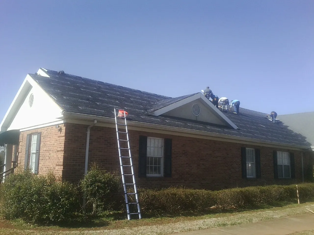 Crew tearing shingles off a brick ranch roof with a ladder set — Metal Roof Repair work by our crew in Veedersburg