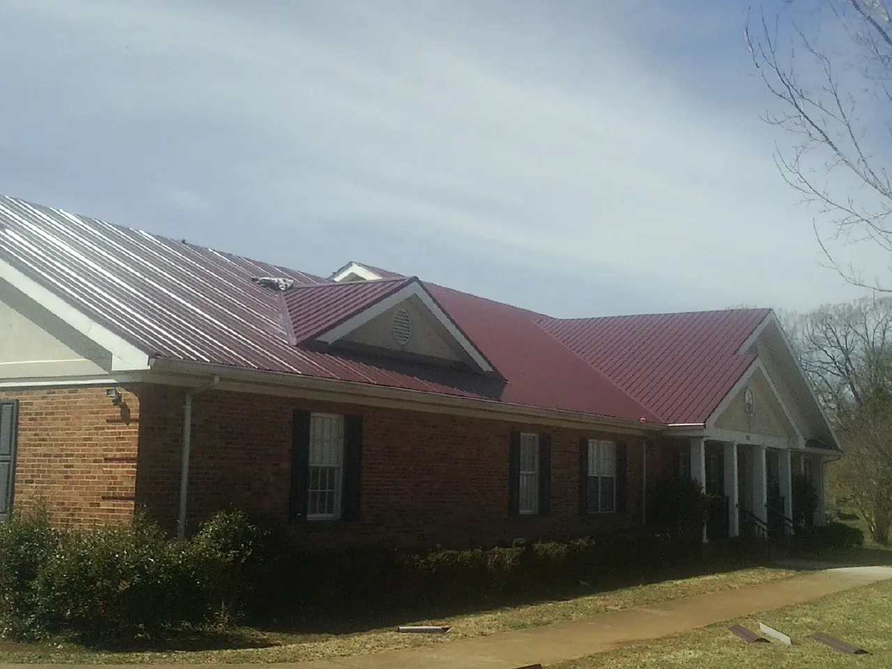 Red metal roof with gabled entries on a long brick building, from a Hail Damage Roof Repair job in Veedersburg