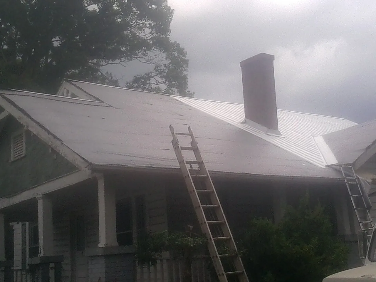Ladders against a metal roof on an older home with a brick chimney in Veedersburg