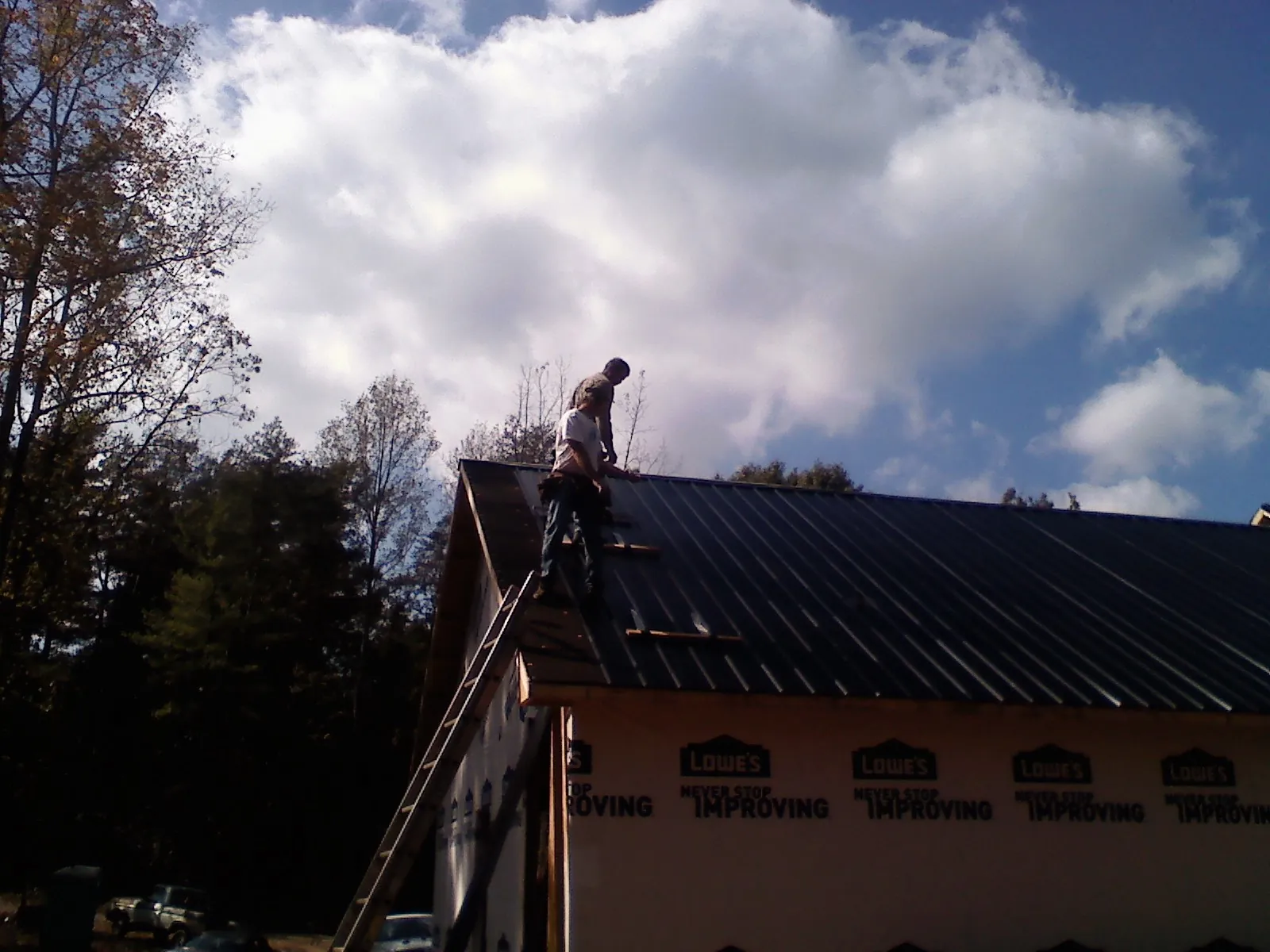 Roofer fastening dark metal panels high against a cloudy sky, from a Roof Inspection job in Veedersburg