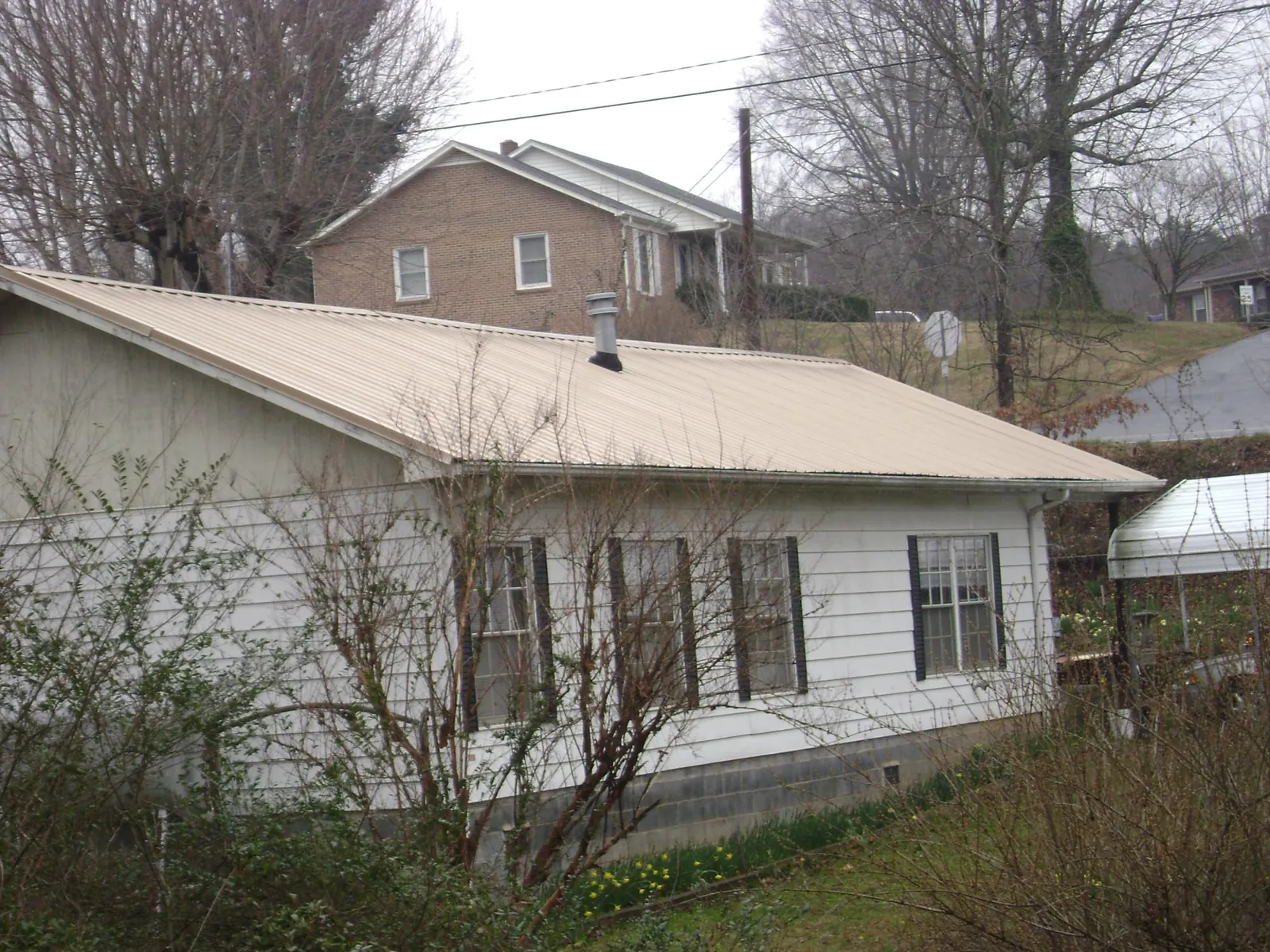 Tan metal roof on a white sided house set into a hillside — Commercial Roofing by Roofing Brothers in Veedersburg